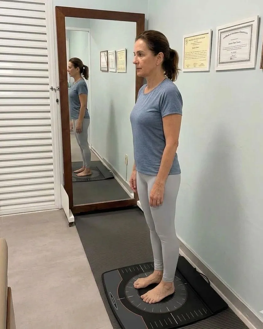 Paciente em avaliação postural sobre a plataforma, de perfil ao espelho